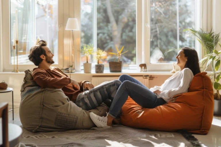 Pareja relajada conversando en un ambiente acogedor, sentados en sillones puff en una sala soleada, fomentando una comunicación abierta y efectiva.