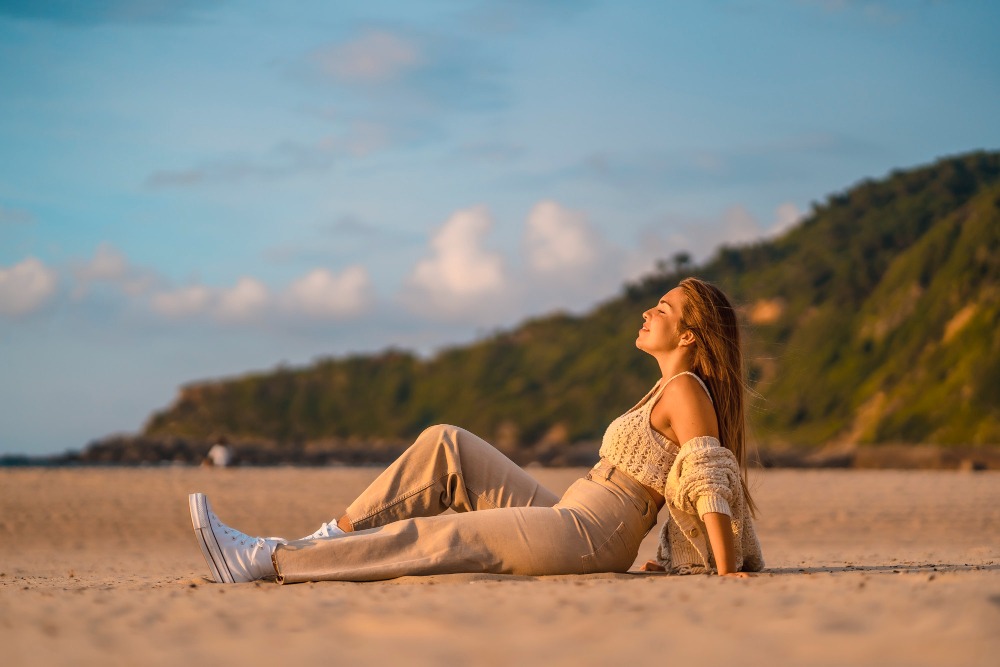 Mujer sentada en la playa disfrutando de un momento de relajación bajo el sol, representando calma y control sobre la ansiedad